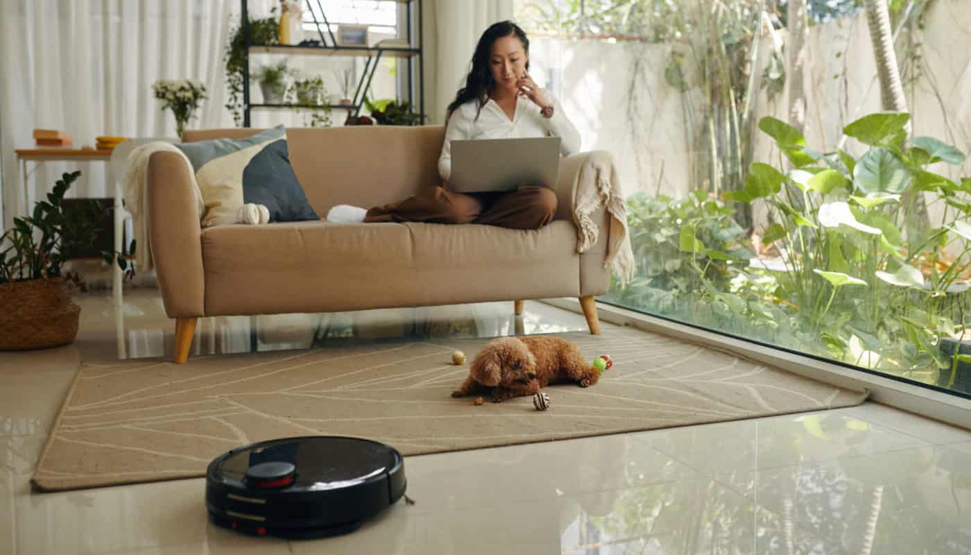 woman-uses-laptop-while-home-cleaning-robot-works Robotic Vacuums vs Traditional Cleaning
